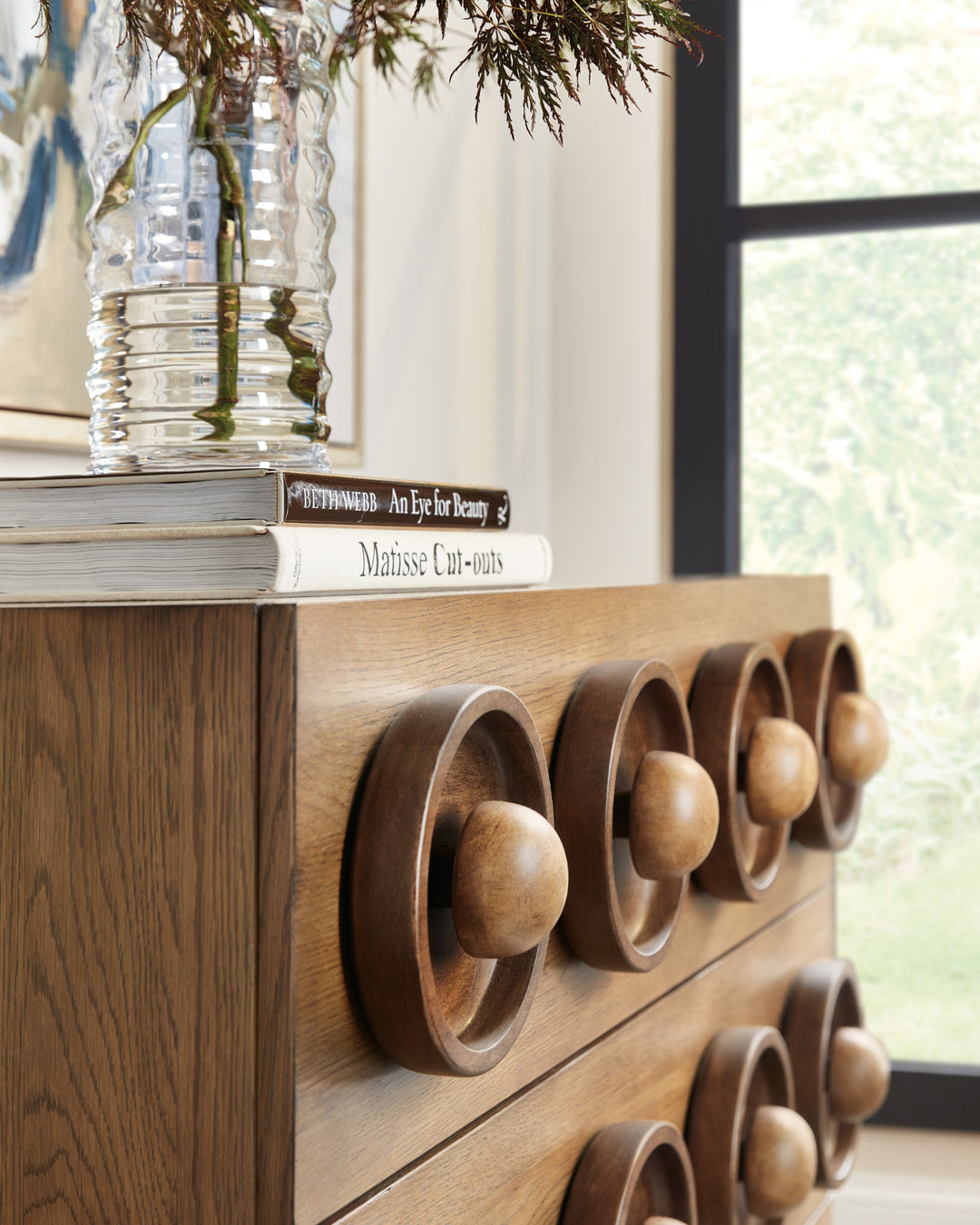 Close up of a wooden drawer chest with a geometric design featuring three rows of circular, recessed patterns and spherical knobs.