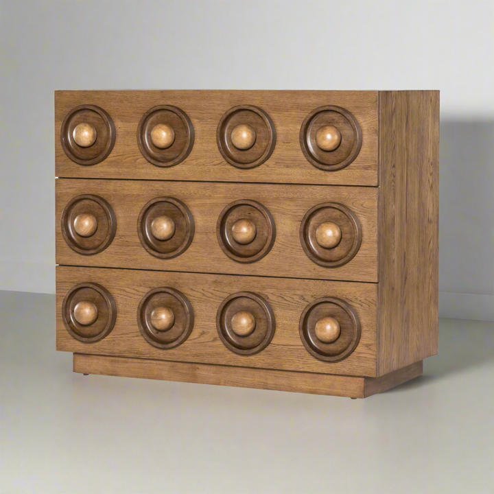 Angled view of a wooden drawer chest with a geometric design featuring three rows of circular, recessed patterns and spherical knobs.