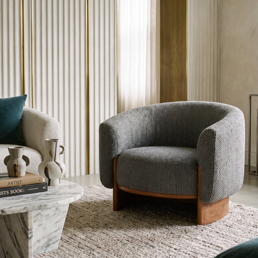 Modern living room featuring a textured gray barrel chair, marble coffee table, and elegant fluted wall paneling.