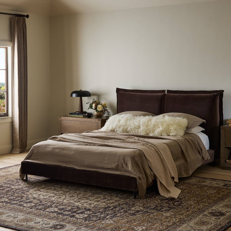 Cozy bedroom featuring a brown meadow cocoa velvet upholstered bed, neutral linens, a fluffy throw, wooden nightstands.