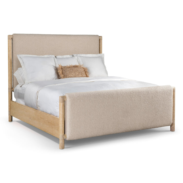 Side view of a bed with a light wood frame and beige upholstered headboard and footboard. Dressed with white bedding and features a single textured brown accent pillow.