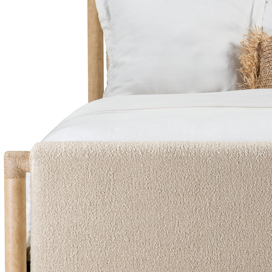 Close up short of a beige upholstered bed with wooden frame, white bedding, and a textured tan pillow.