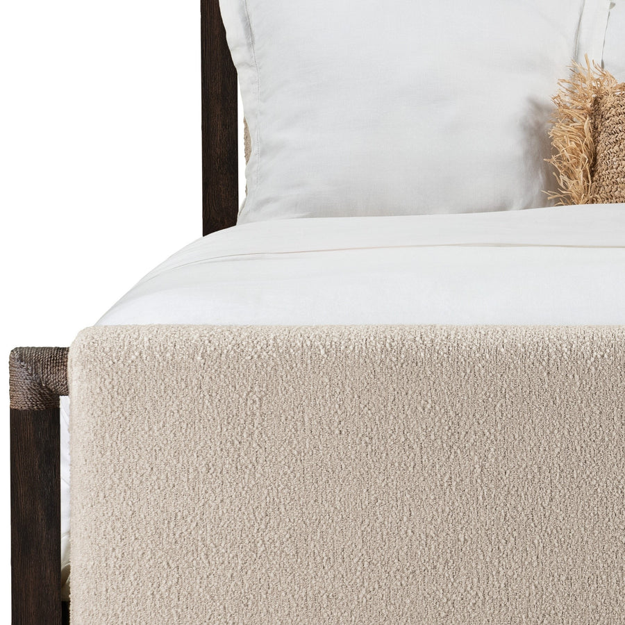 A close-up of a upholstered panel bed featuring a soft beige textured bed frame, white bedding, and a decorative throw pillow.