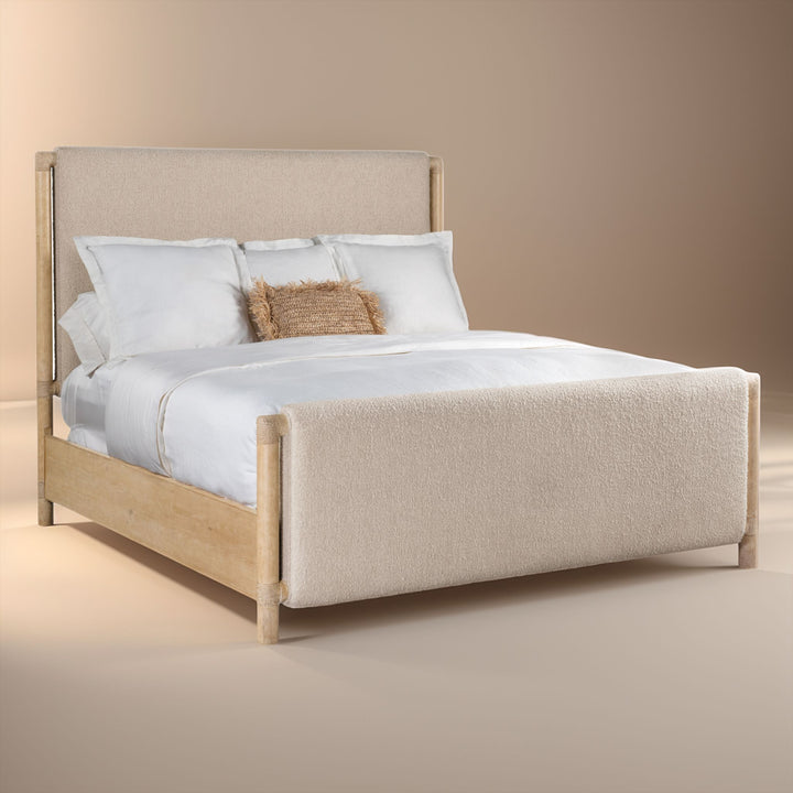 Side view of a bed with a light wood frame and beige upholstered headboard and footboard. Dressed with white bedding and features a single textured brown accent pillow.