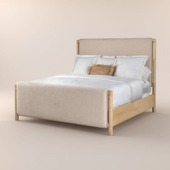 Side veiw of a bed with a light wood frame and beige upholstered headboard and footboard. Dressed with white bedding and features a single textured brown accent pillow.