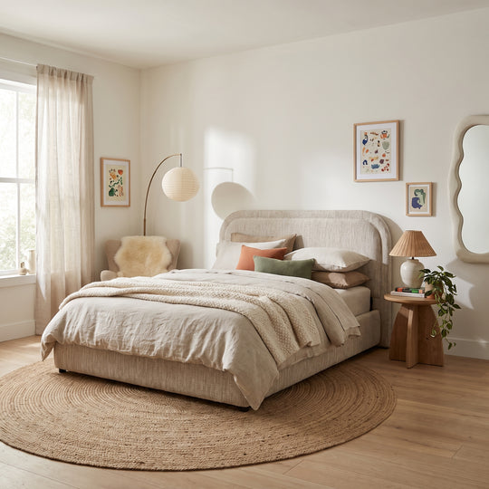 Cozy modern bedroom with a beige upholstered bed, round jute rug, warm lighting, and minimalist neutral decor.