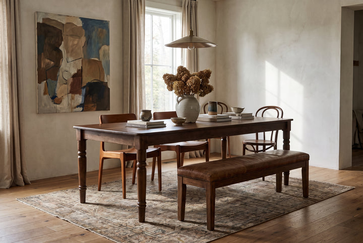 The Russet Dining Table in a warm, rustic dining room with a leather bench, wooden chairs, and neutral decor.