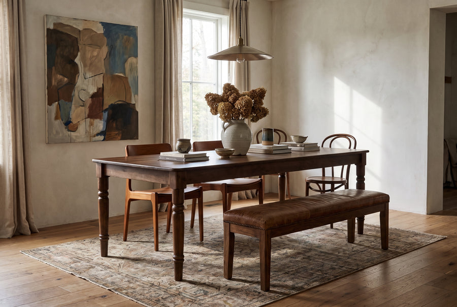 The Russet Dining Table in a warm, rustic dining room with a leather bench, wooden chairs, and neutral decor.