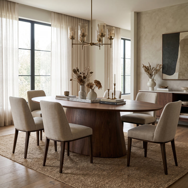 Modern dining room with a walnut oval table, beige upholstered chairs, and a brass chandelier in a minimalist, neutral space.