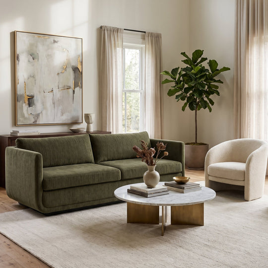 Modern living room with an olive green sofa, marble coffee table, cream accent chairs, and abstract wall art in a bright space.