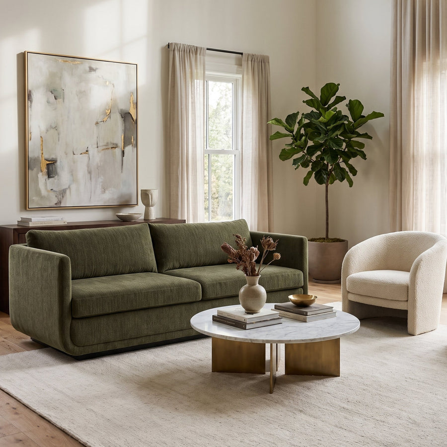 Modern living room with an olive green sofa, marble coffee table, cream accent chairs, and abstract wall art in a bright space.