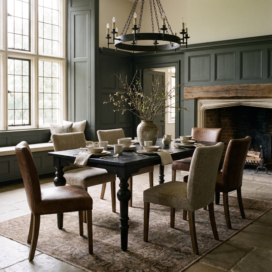 Elegant dining room with dark green paneled walls, a rustic wooden table, upholstered chairs, and a classic iron chandelier.