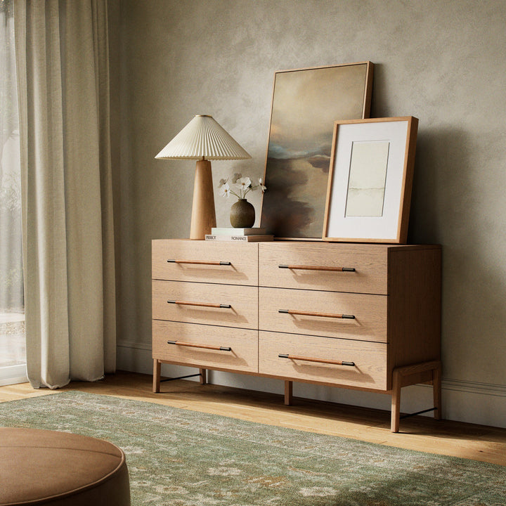 A stylish rosedale wooden dresser with six drawers, a table lamp, framed art, and a vase with flowers against a textured wall.