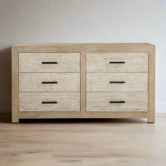 Wooden dresser with four drawers on a wooden floor against a plain wall.