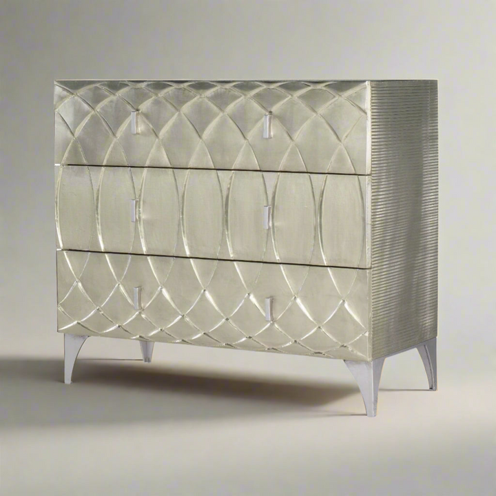 Silver three-drawer dresser with a textured, overlapping oval pattern on the front, featuring sleek metal handles and tapered legs.